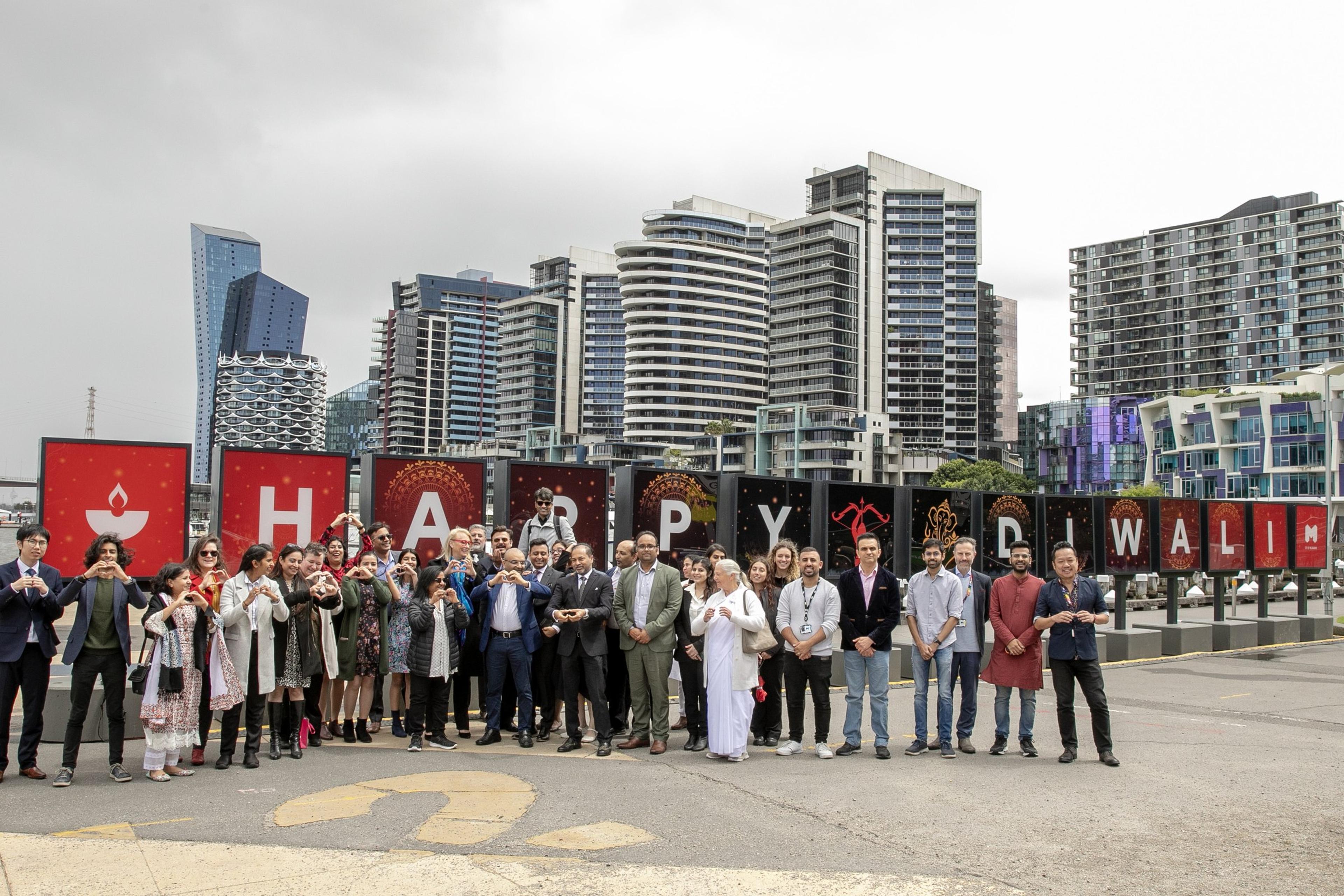 A group making heart signs in front of giant HAPPY DIWALI letters on the Docklands waterfront, Melbourne