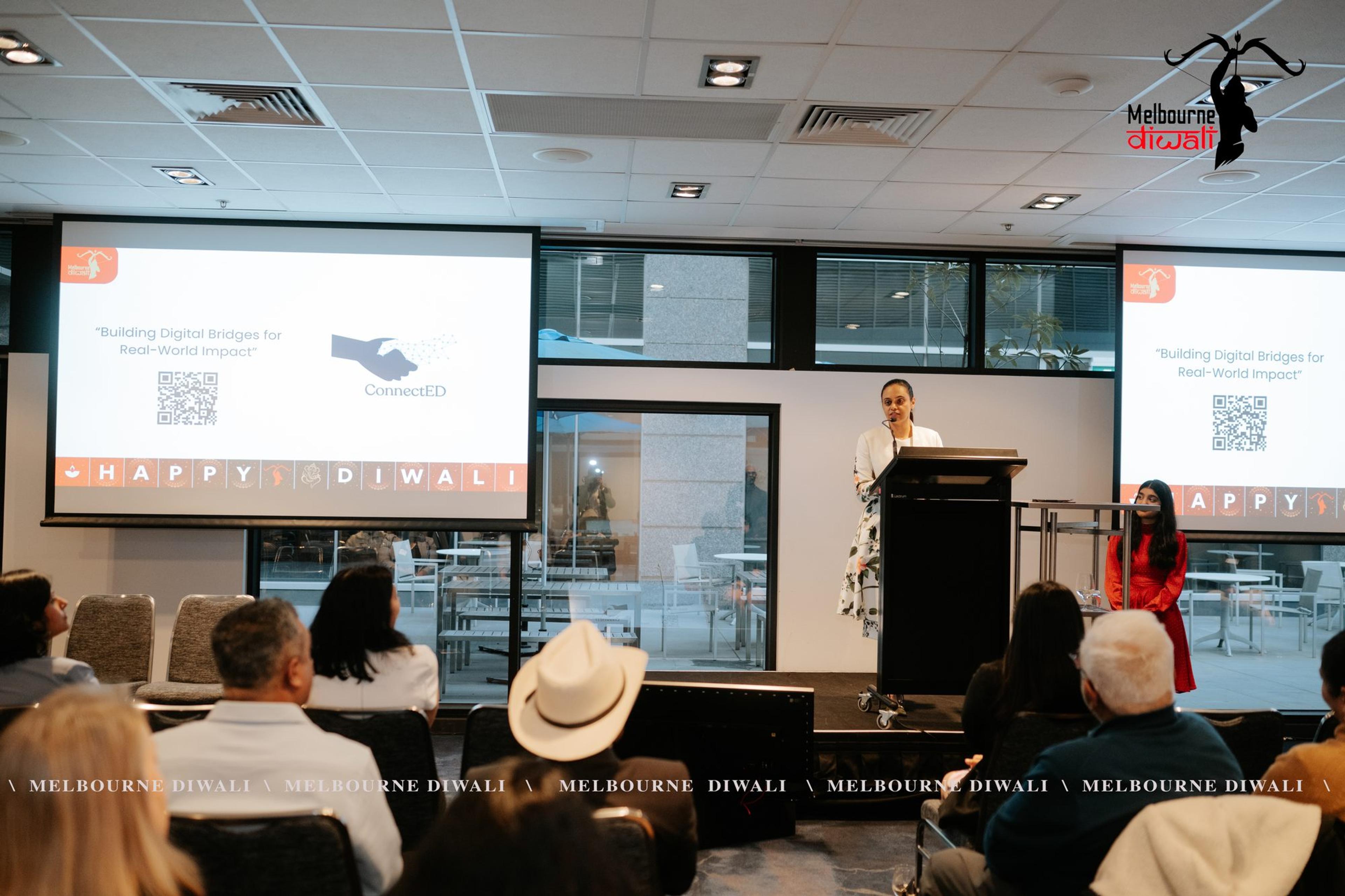 Dr Reet Kaur presents ConnectED at the lectern beside the slide 'Building Digital Bridges for Real-World Impact'