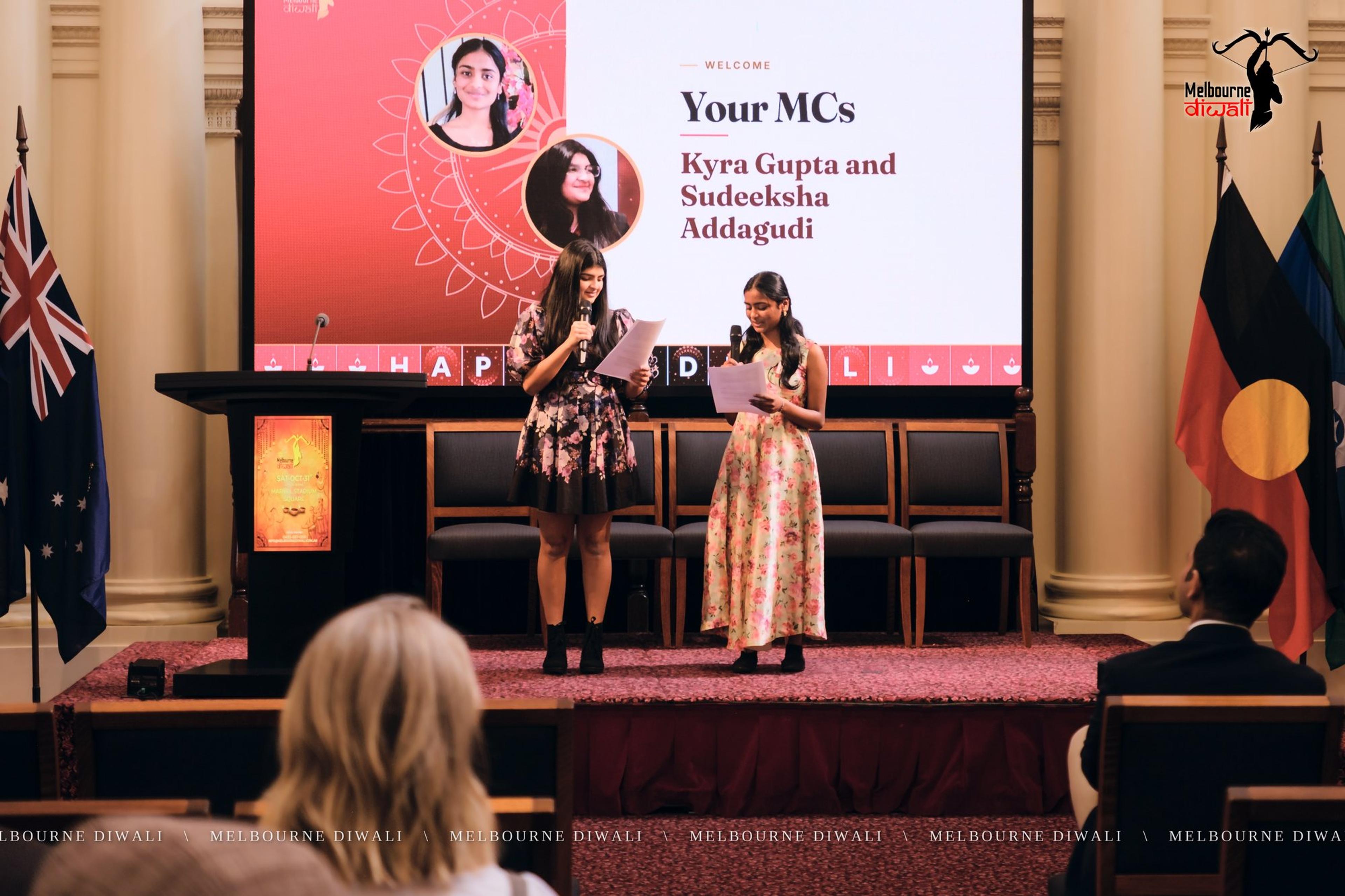 The MCs, Kyra Gupta and Sudeeksha Addagudi, welcome guests beside their name slide