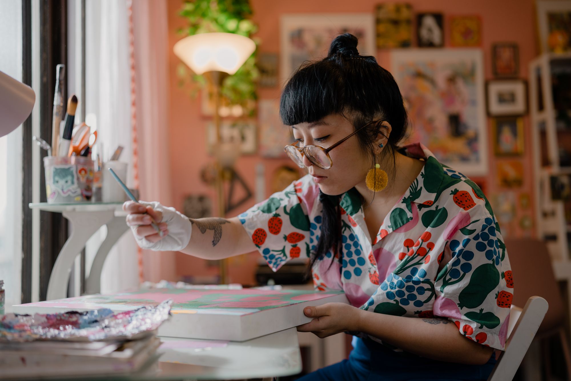Candid photograph of painter and illustrator Kristen Liu-Wong working on a new painting in her home studio. 