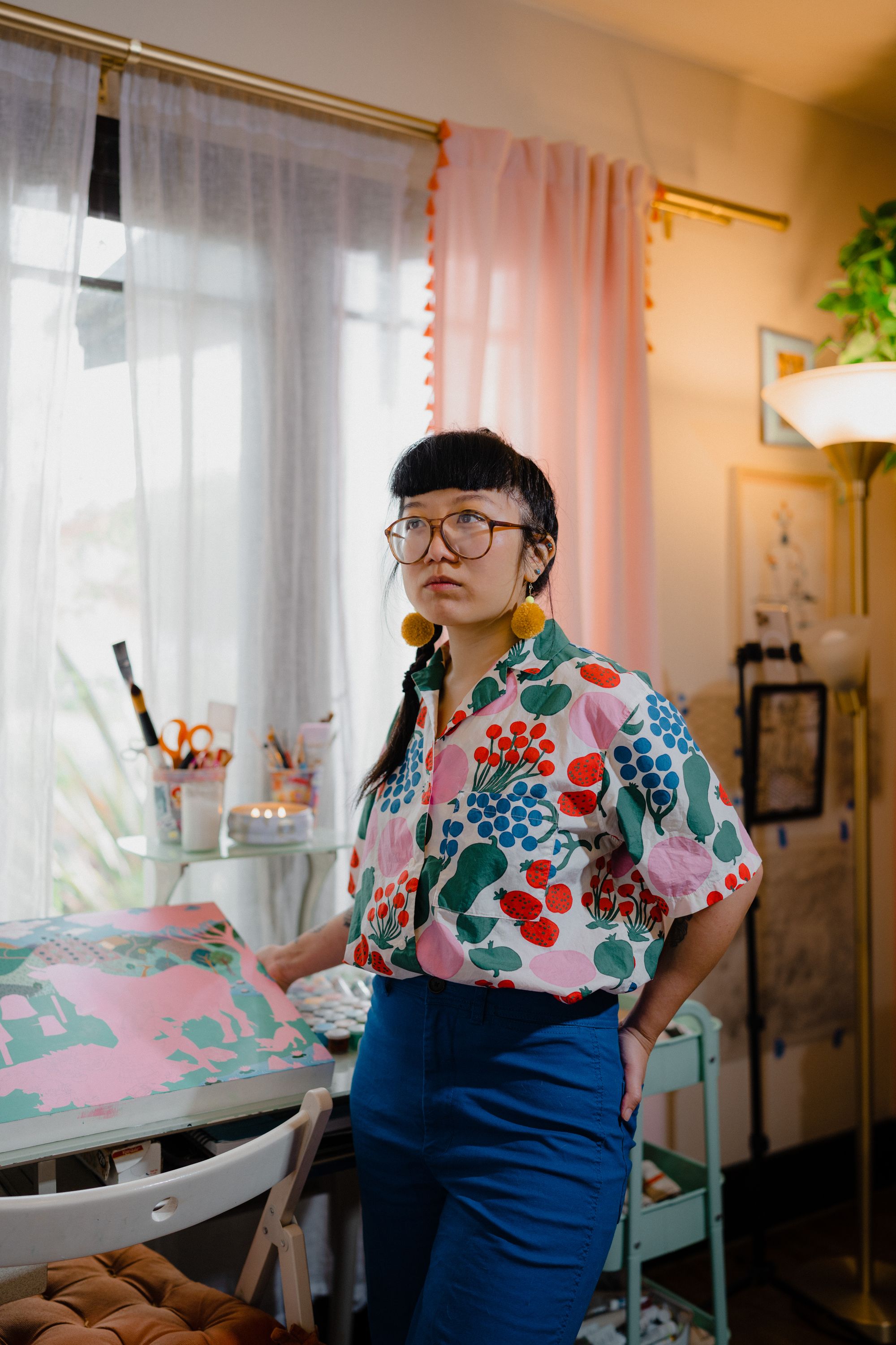 Photographic portrait of painter and illustrator Kristen Liu-Wong standing in her home studio showing her latest painting in progress.