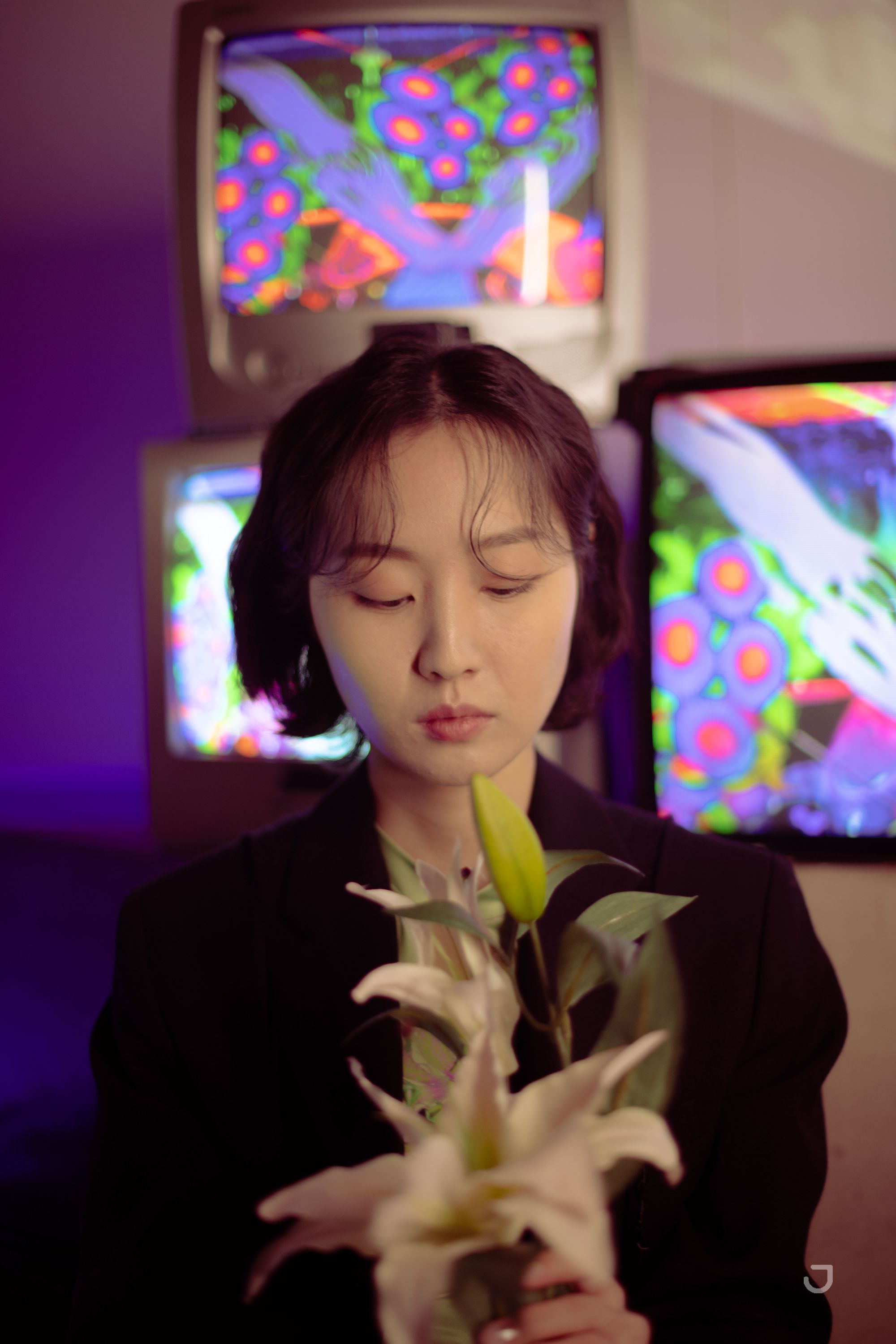 Artist Ram Han with flowers in front of retro TVs with her work on them