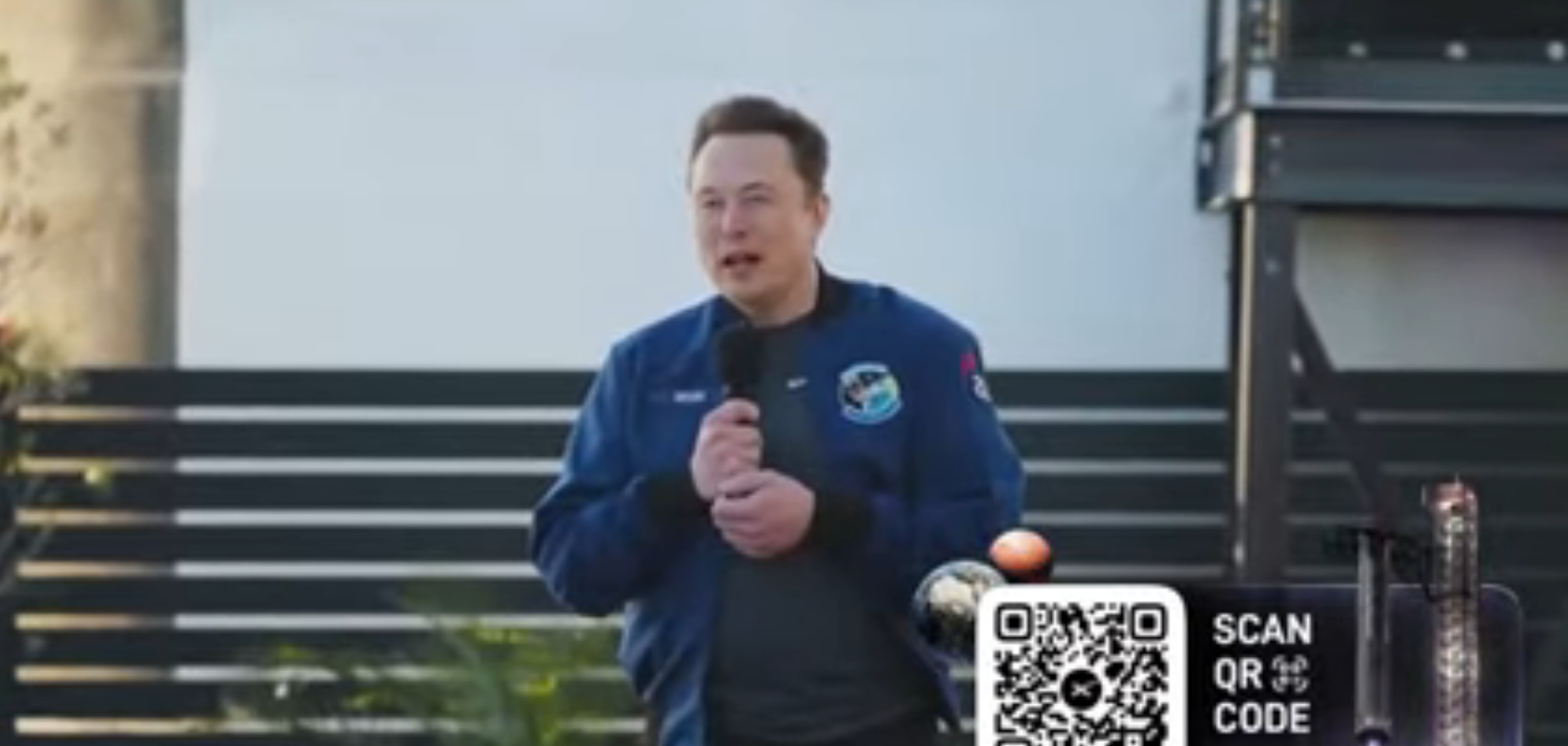 Image of Elon Musk standing holding a microphone in a frame from the SpaceX crypto scam