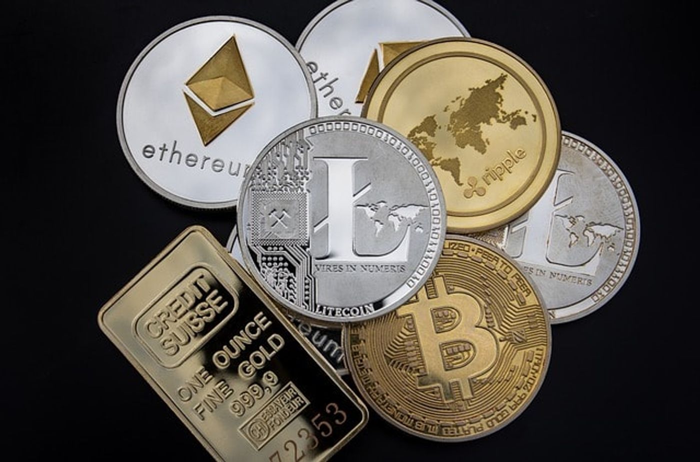 Eight crypto coins, in silver and gold colors, with different cryptocurrency logos such as Bitcoin and Ethereum, one on top of the other, unorderly