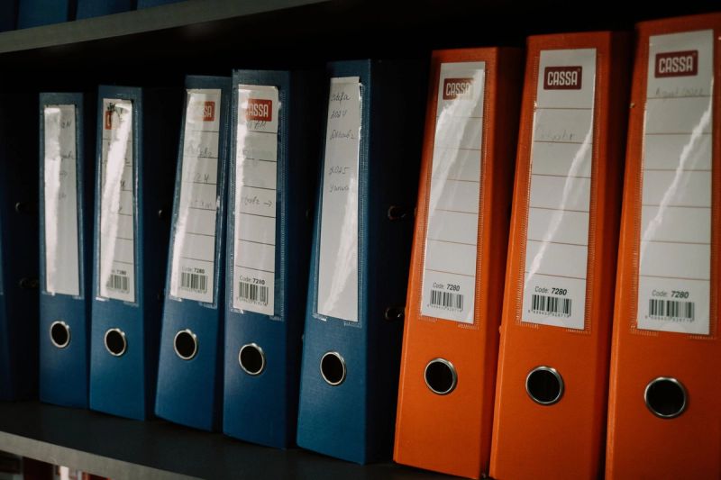 Des classeurs bleus et orange alignés et étiquetés sur une étagère.