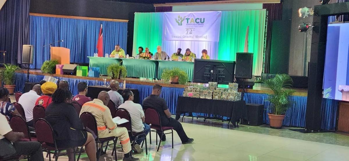 Wide view of the 72nd AGM stage with TACU banner, board members at head table, and members seated in the auditorium