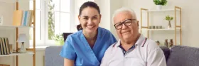 A caregiver and a senior smiling while sitting on a couch