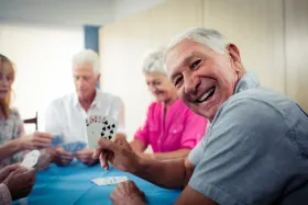 Elderly man plays cards with friends around a table.