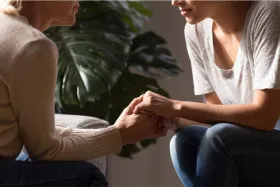 Young woman holding her mother's hands and speaking to her about moving to a memory care facility.