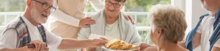 A group of seniors converse around an assisted living dining table