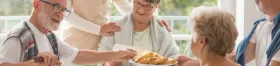 A group of seniors converse around an assisted living dining table