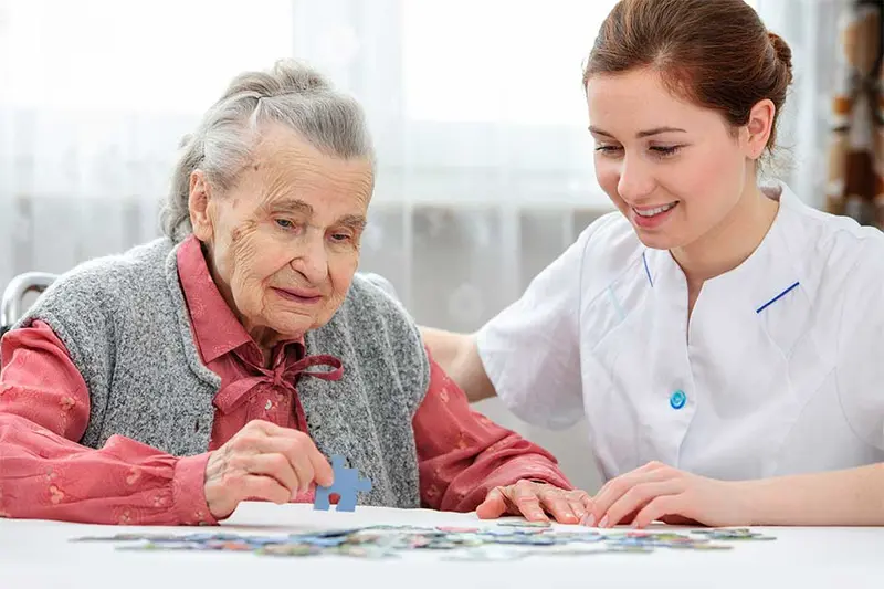 Elderly woman putting together a puzzle with the help of a caregiver