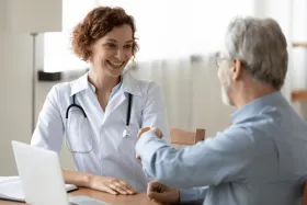 A doctor and senior man talk at a desk.