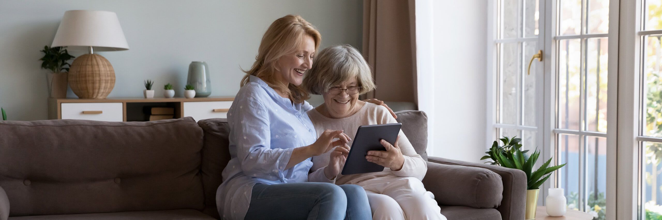 An in-home caregiver looking at a tablet with a senior woman while smiling