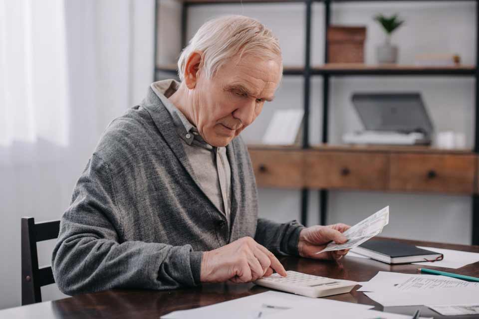 Elderly man at his desk doing calculations by hand and paying medical bills.
