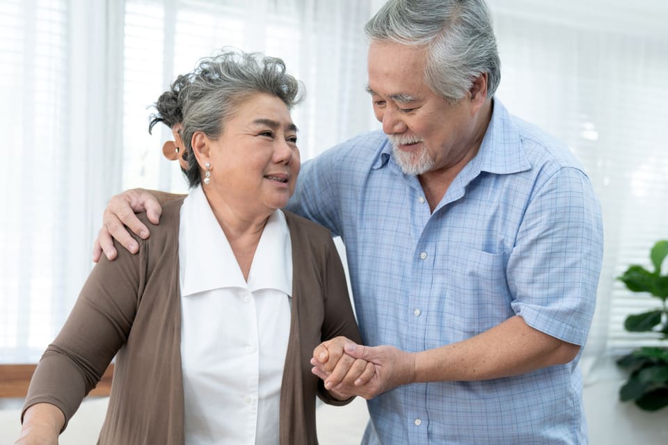 Older Asian couple walking, man has arm around her shoulder