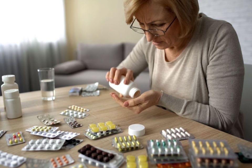 A senior woman looking distressed at a table full of various medications