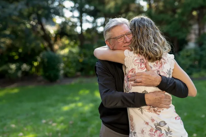Older father embraces his adult daughter outdoors, representing the family relationships behind decisions about paying for senior care.