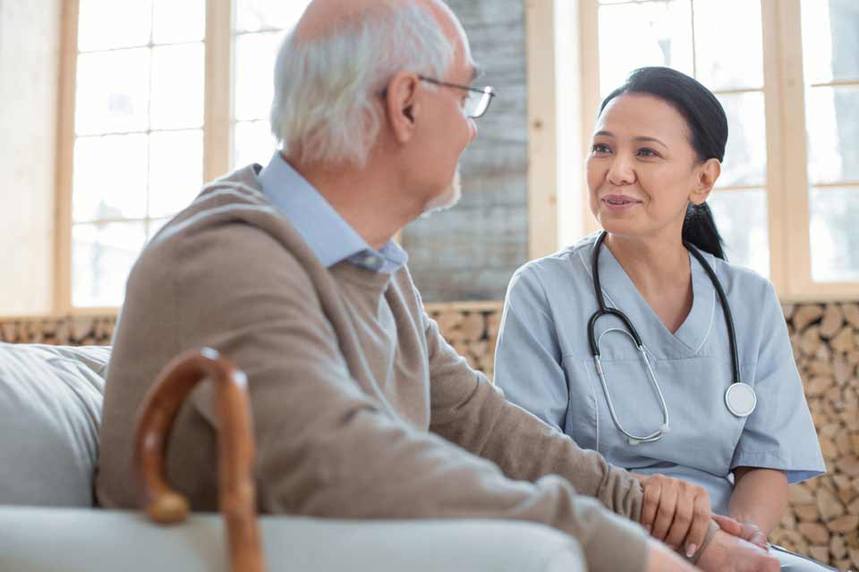 Elderly man with a cane and his caregiver in a nursing home having a conversation.