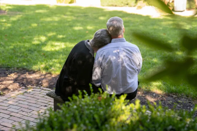 Two seniors sitting next to each other, embracing and facing away from the camera. 