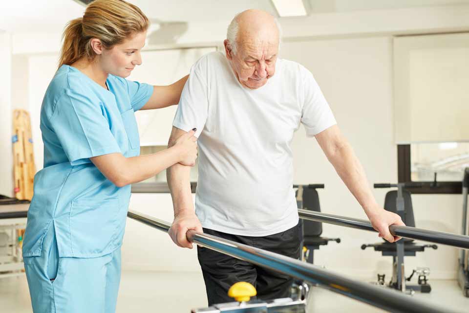 Nurse helping an elderly man with his ability to walk using bars.