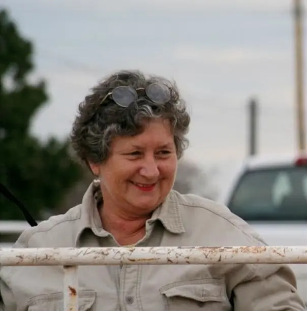 Martha smiles while standing by a white fence at a horse stable.