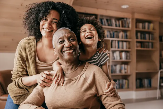 Older woman smiles with her adult daughter and grandchild, representing the central role women play in caregiving across generations.