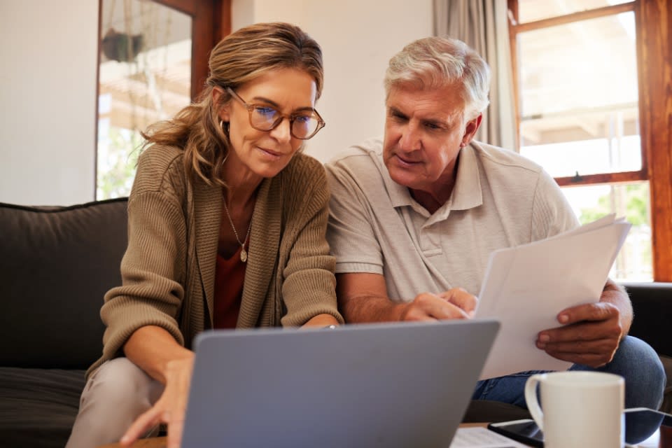 Smiling, contemplative older couple looks at a computer while deciding how to pay for independent living