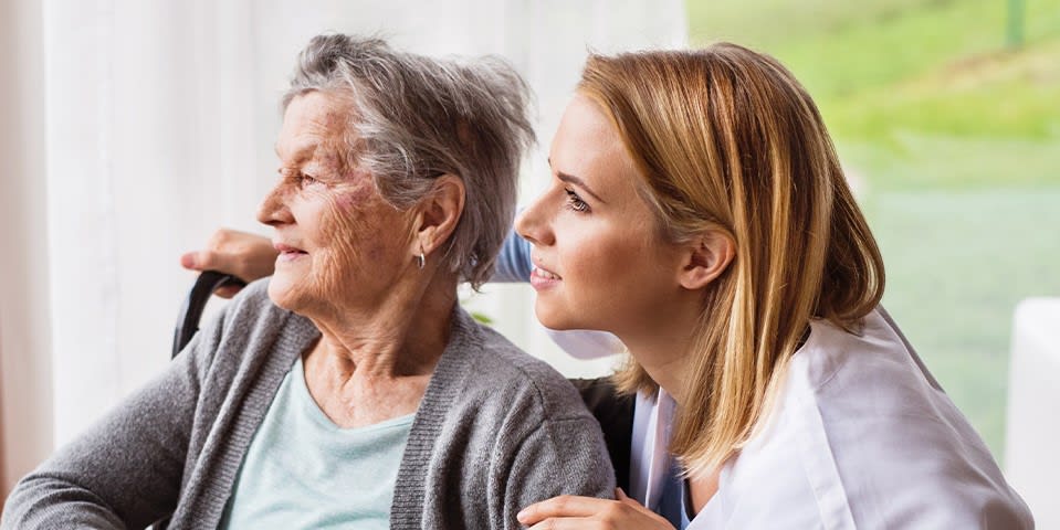 Older woman sits smiling gently with younger woman behind her, looking over her shoulder