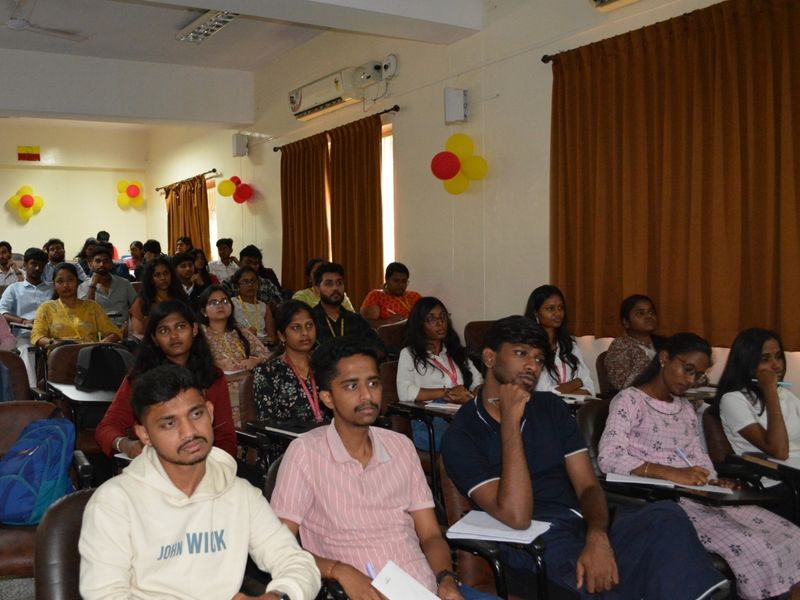 Audience members and students seated in rows inside an auditorium, attentively watching a presentation during a pharmacovigilance workshop with balloons decorated in the background.