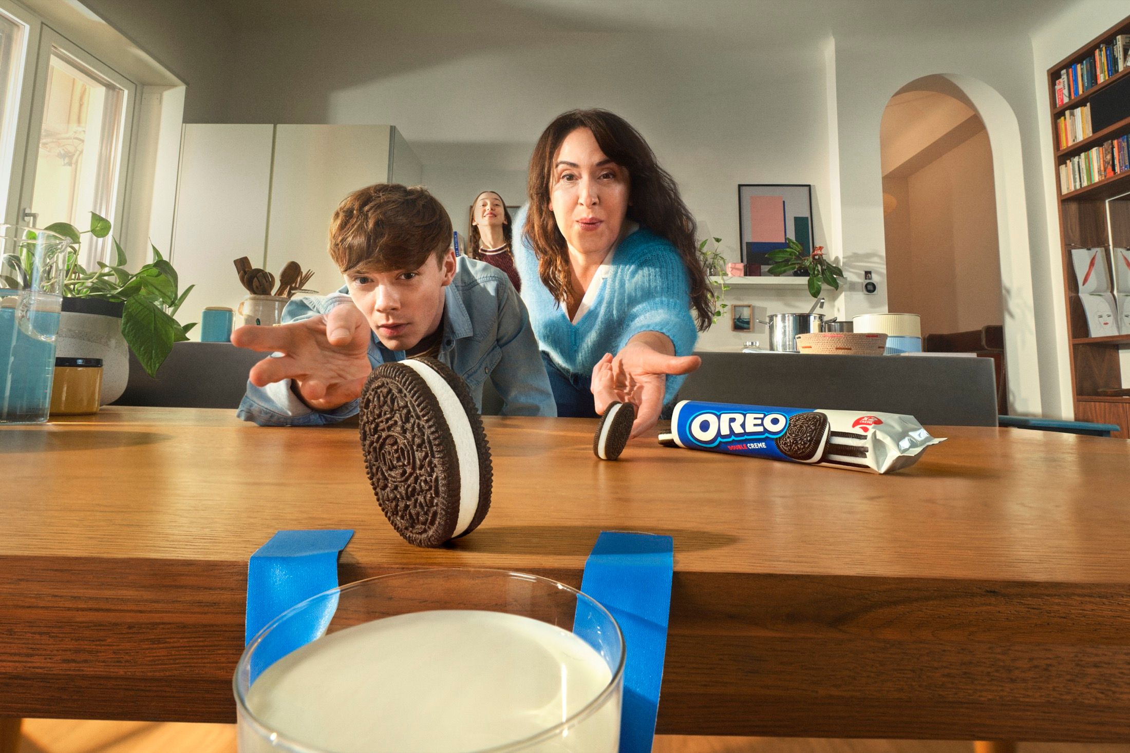 Oreo campaign image of a mother and son rolling Oreo cookies across a wooden table toward a glass of milk.