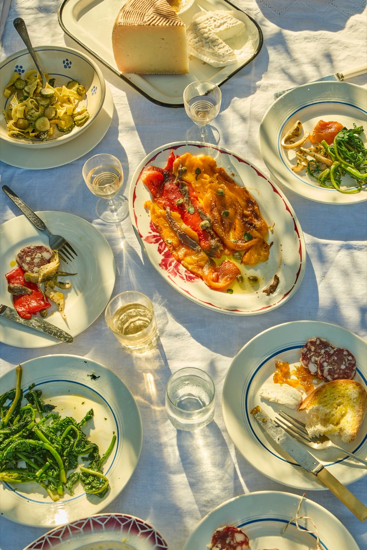 Overhead sunlit Italian table of antipasti, cheese, roasted peppers and wine, shot for Theo Randall's The Italian Table.