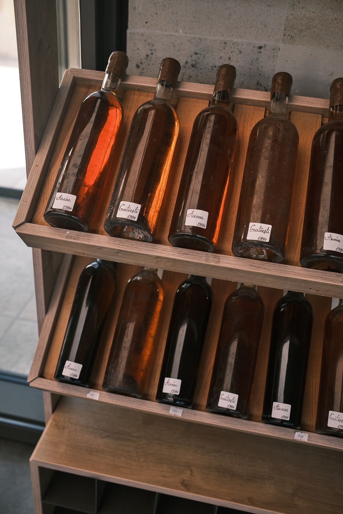 Hand-labelled bottles of amber and orange wine lying on tilted wooden display racks at Plincuvin.