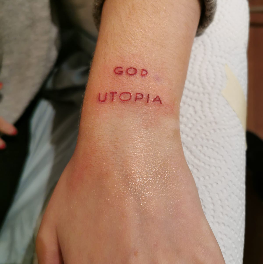 a woman's wrist with a cover-up tattoo saying go to utopia, berlin, germany