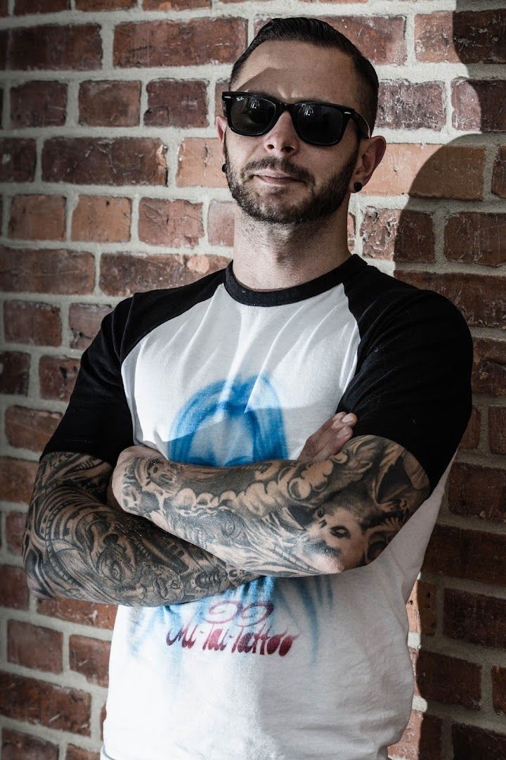 a man with narben tattoos standing in front of a brick wall, rostock, germany
