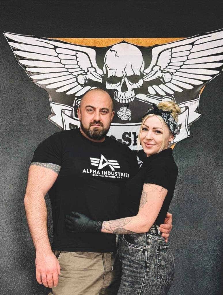 a man and woman posing for a photo in front of a wall with a skull on it