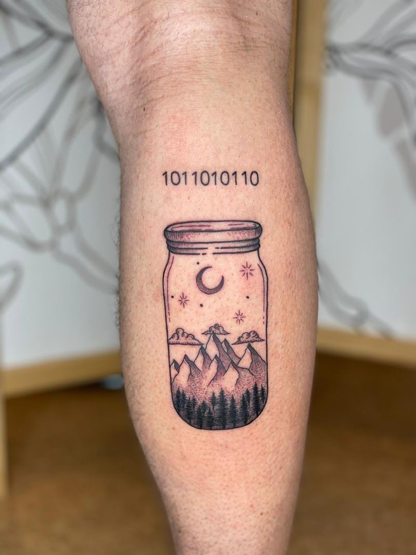 a man's forearm with a mountain scene in a jar