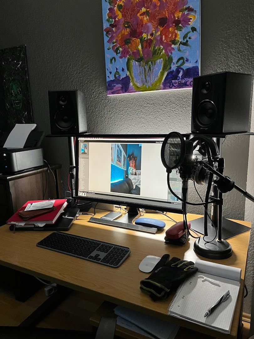 a desk with a computer, speakers, and a painting