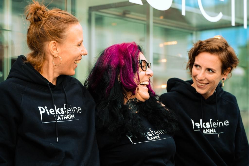 three women in black hoodies with pink hair and black glasses