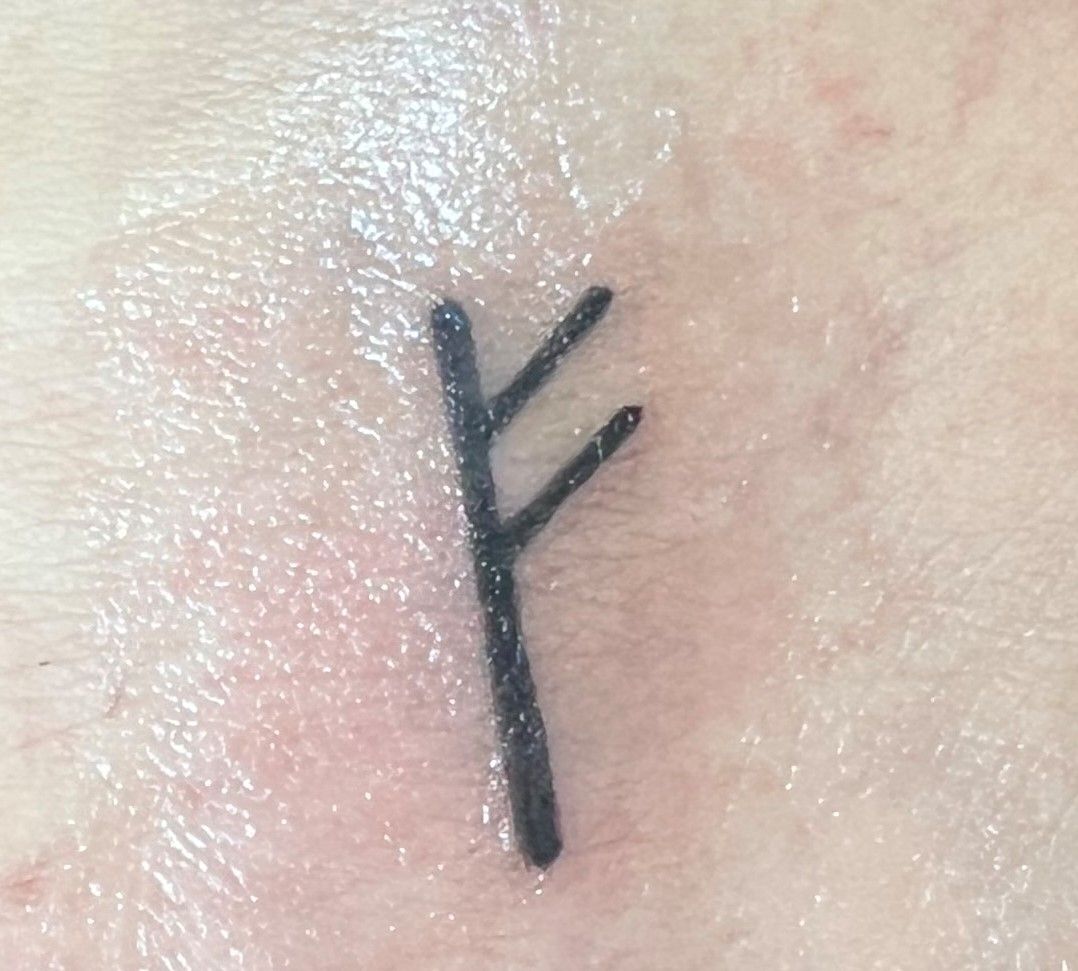 a close up of a person's arm with a small black cross on it