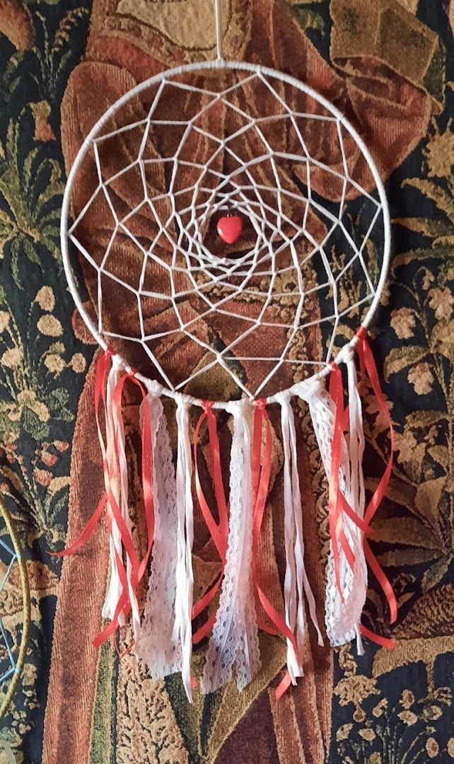 a white dream catcher with red ribbons and a red heart