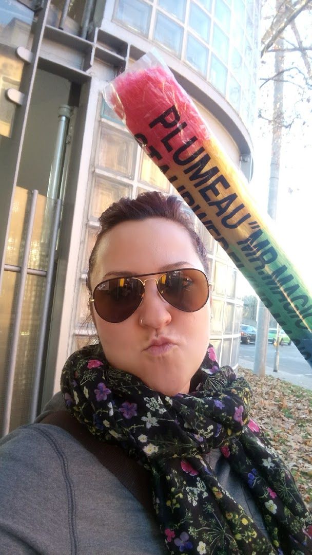 a woman wearing sunglasses and a scarf holding a giant pencil