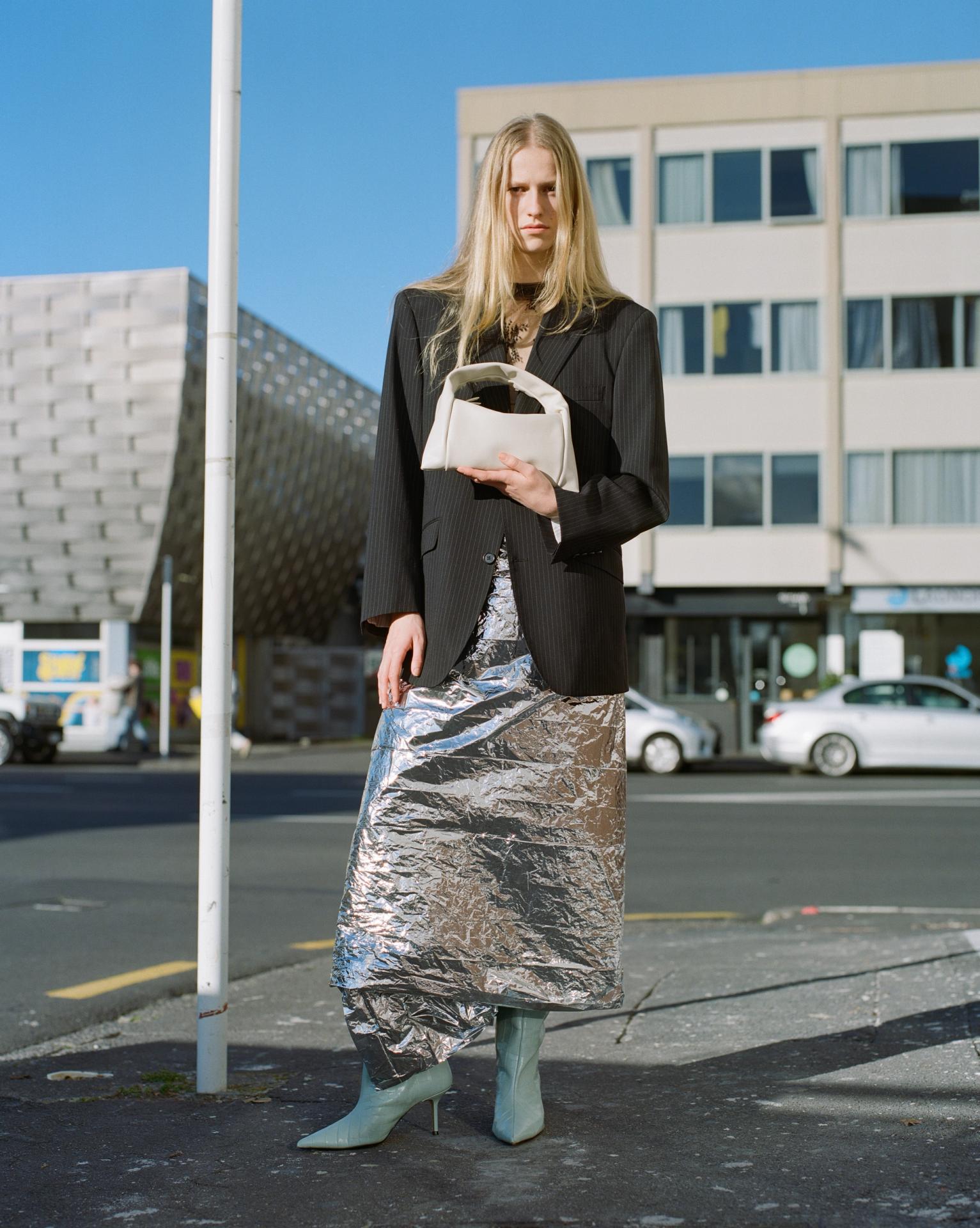a woman in a white shirt and snakeskin skirt is holding a brown bag