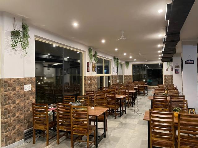 Indoor dining hall with wooden tables and chairs, hanging plants and large windows at Rangmanch Farms, an event and dining venue in Gurugram near Delhi