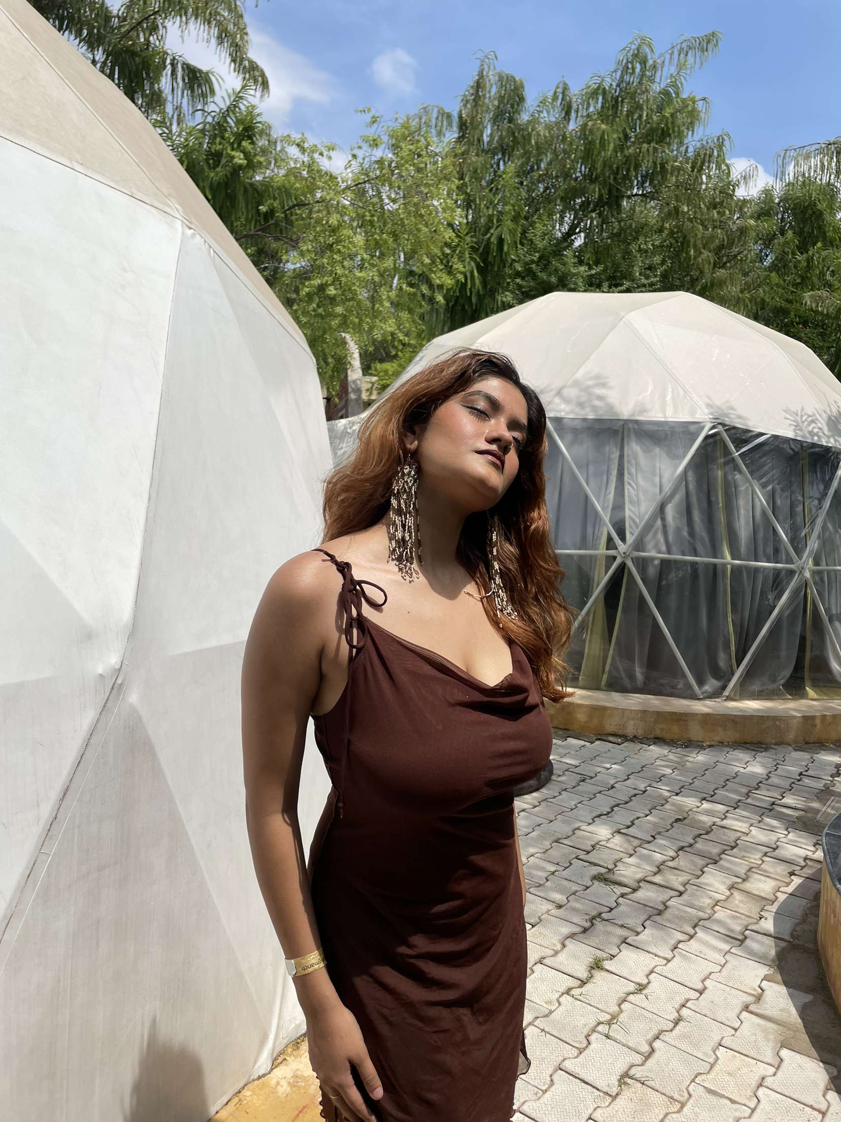 Woman in a brown dress standing beside geodesic glamping domes on a paved courtyard at Rangmanch Farms, an overnight stay venue in Gurugram near Delhi