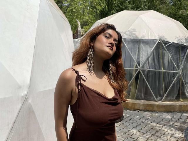 Woman in a brown dress standing beside geodesic glamping domes on a paved courtyard at Rangmanch Farms, an overnight stay venue in Gurugram near Delhi