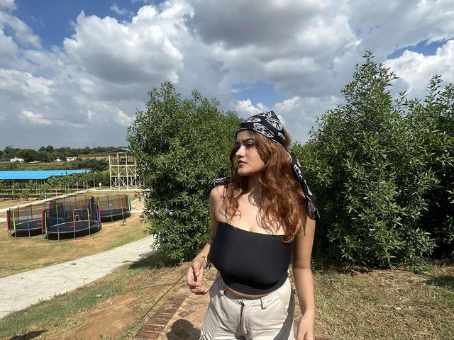 Young woman standing on a brick pathway with trampolines and greenery under a cloudy sky at Rangmanch Farms, an outdoor day outing venue in Gurugram near Delhi