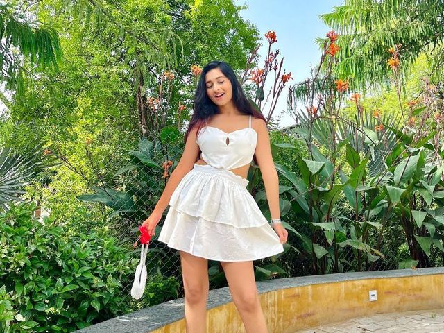 Woman in a white dress posing on a paved path beside greenery and orange flowers in the gardens at Rangmanch Farms, an outdoor event venue in Gurugram near Delhi