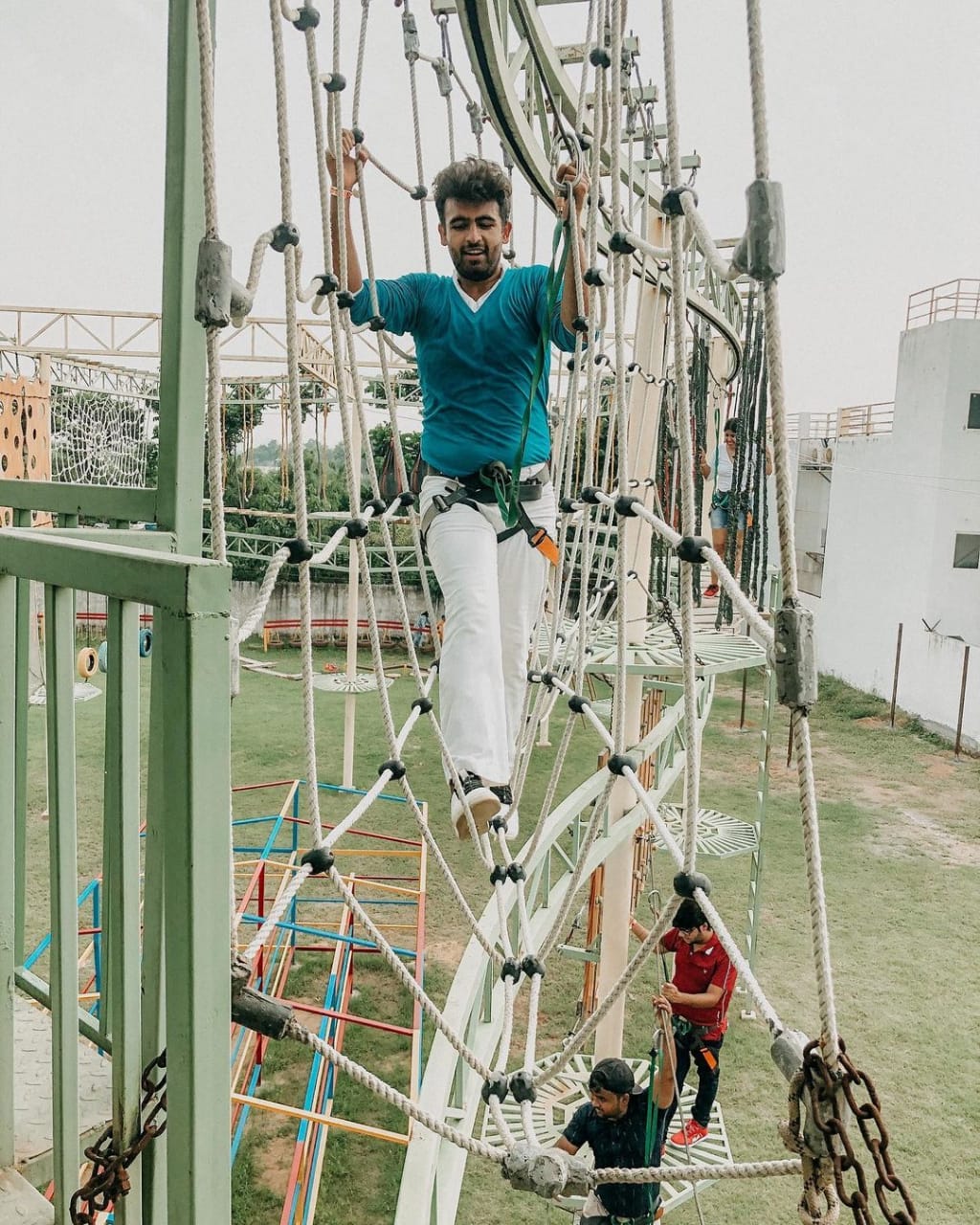 A harnessed man crossing a high ropes obstacle course while others assist below at Rangmanch Farms, an adventure and team building venue in Gurugram near Delhi