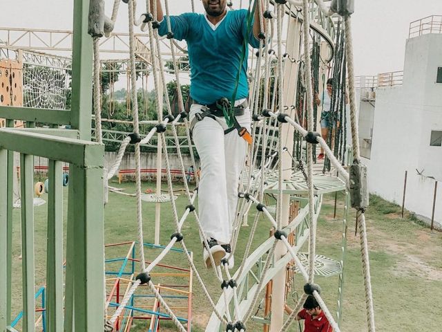 A harnessed man crossing a high ropes obstacle course while others assist below at Rangmanch Farms, an adventure and team building venue in Gurugram near Delhi
